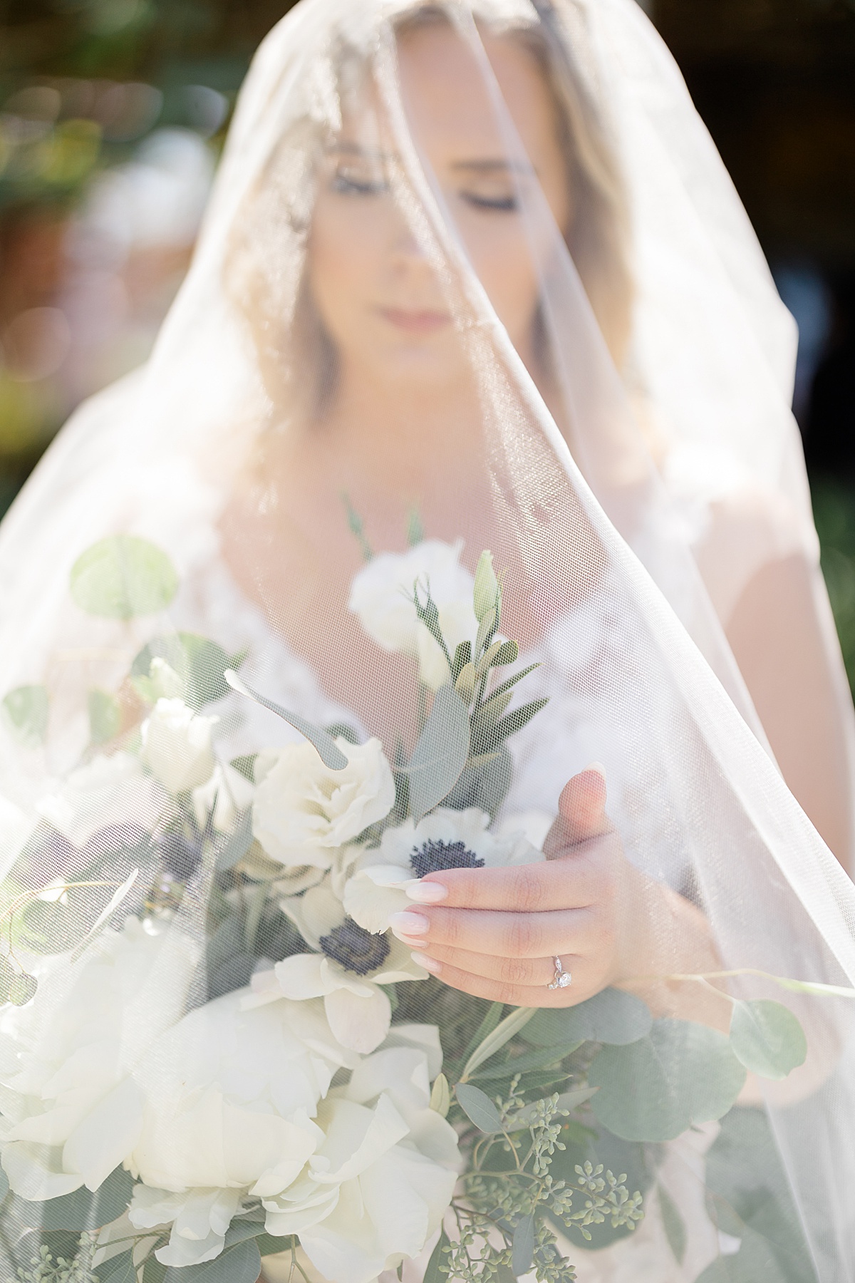 bride with white poppies and greenery bouquet poses under veil before California vineyard wedding