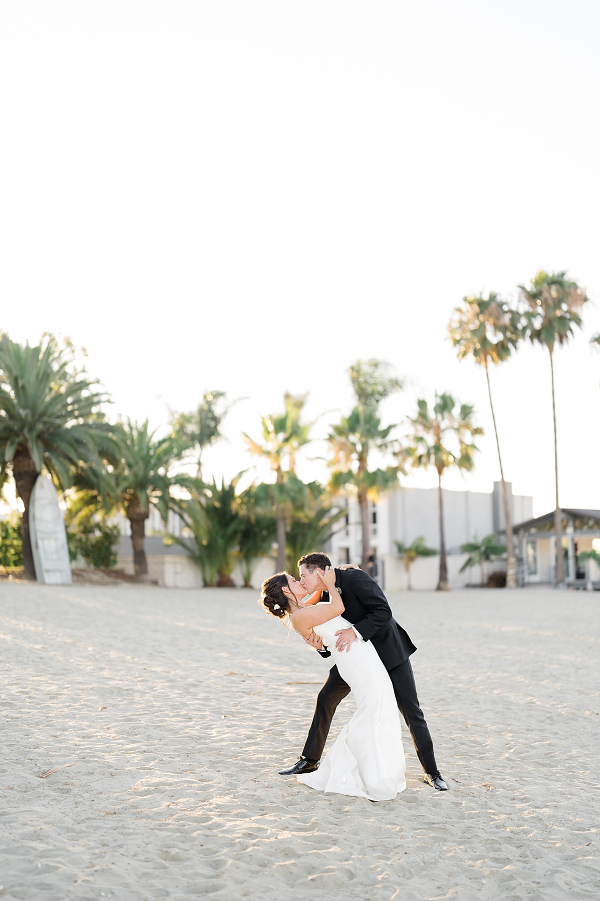 groom dips bride as they kiss with palm trees in background at vow renewal at huntington beach