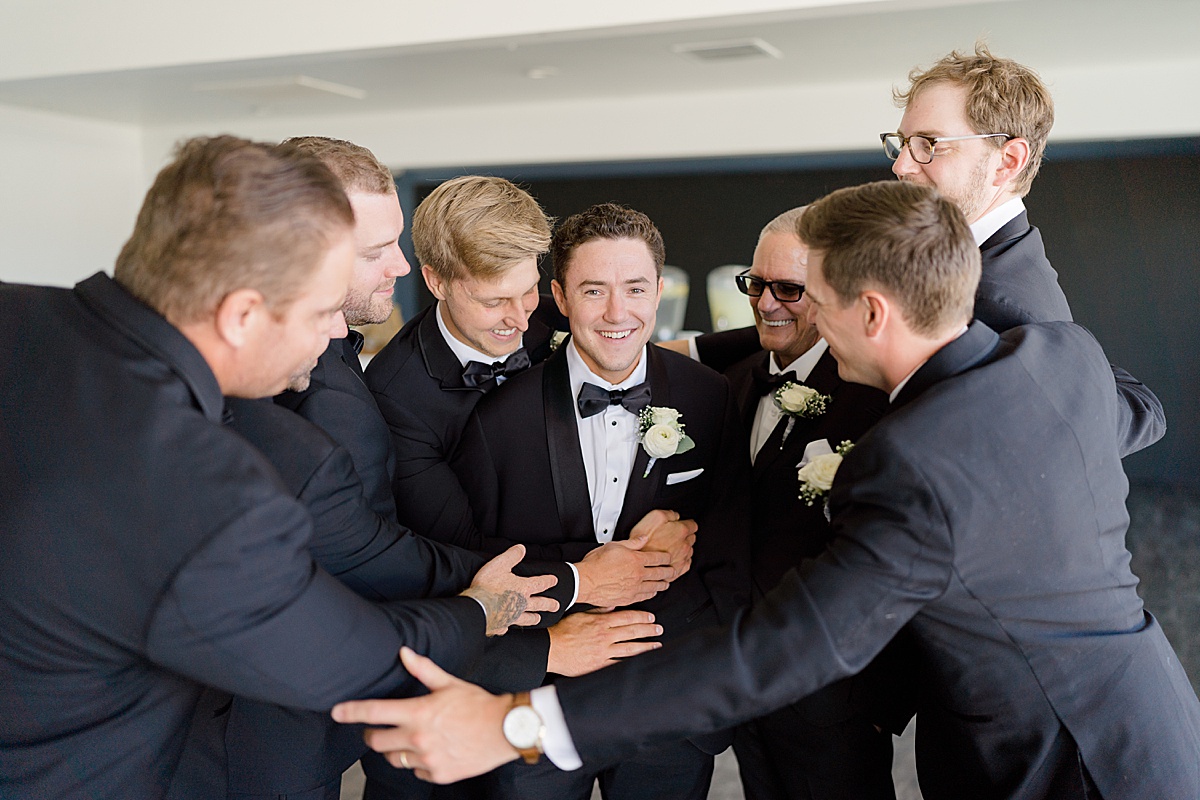 groomsmen in black tuxes congratulate the groom during vow renewal at huntington beach