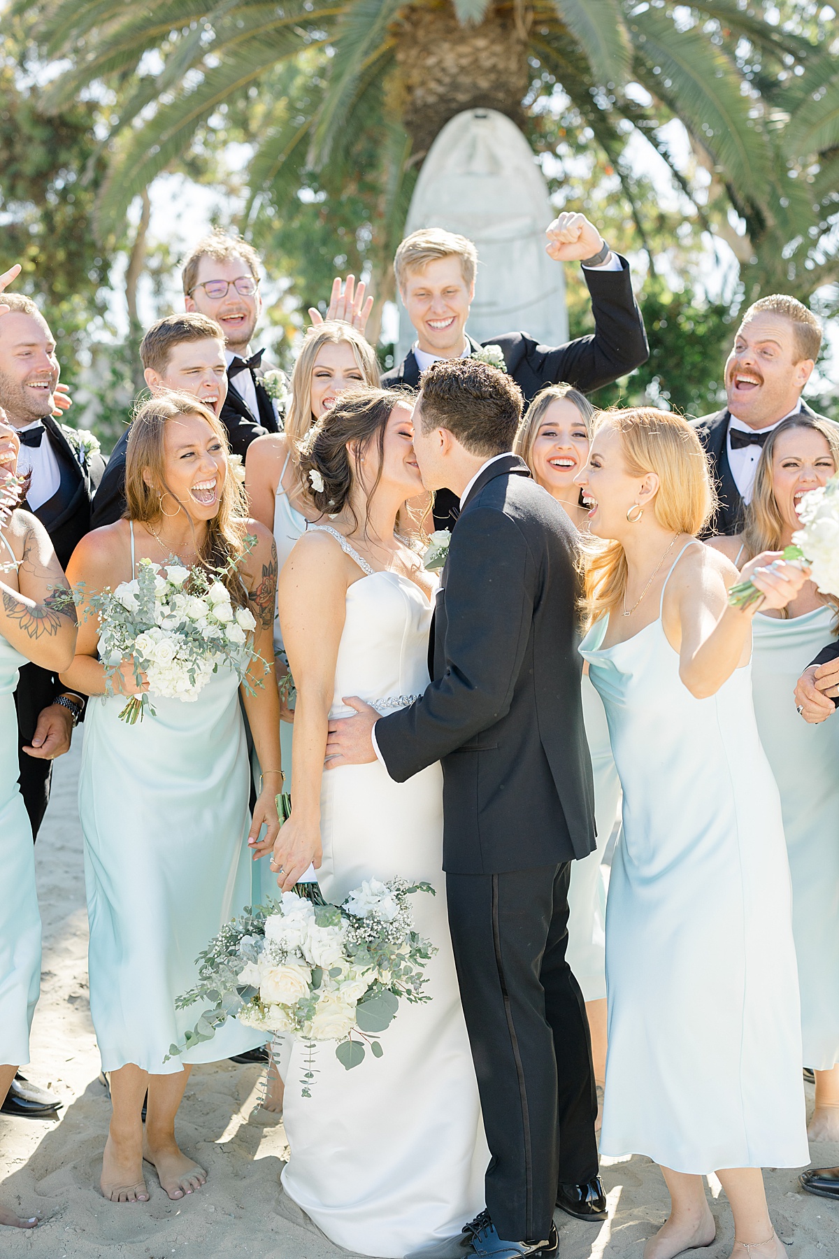 bride and groom kiss as wedding party in pale blue dresses and black tuxes cheer | Hunter Hennes Photography
