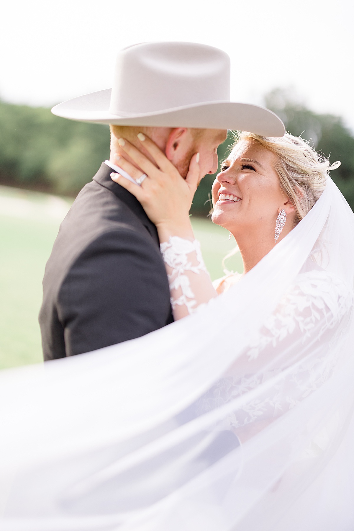bride with diamond earrings and groom in white felt hat smile during Western themed July wedding