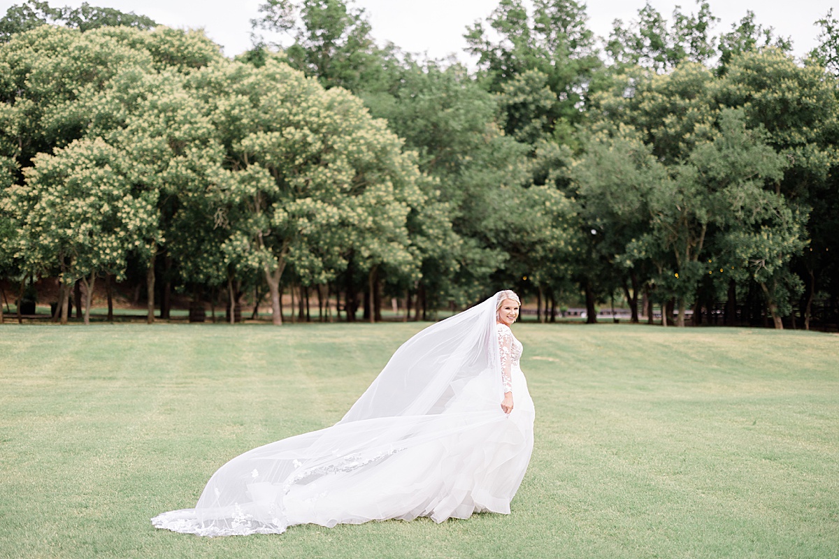 bride with chapel length veil walks across green field during oklahoma ceremony shot by Destination wedding photographer