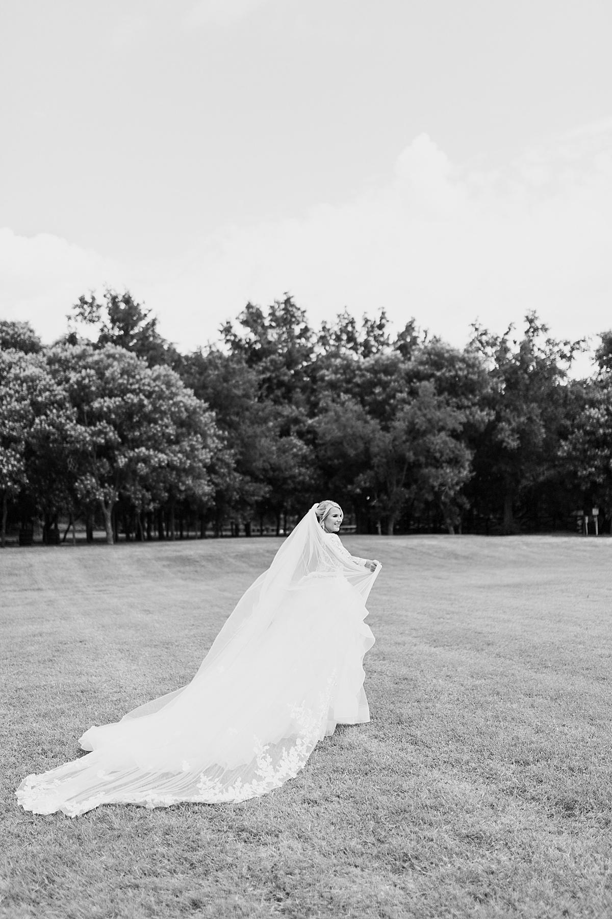 bride with chapel length veil smiles as she walks across a beautiful summer field for Destination wedding photographer