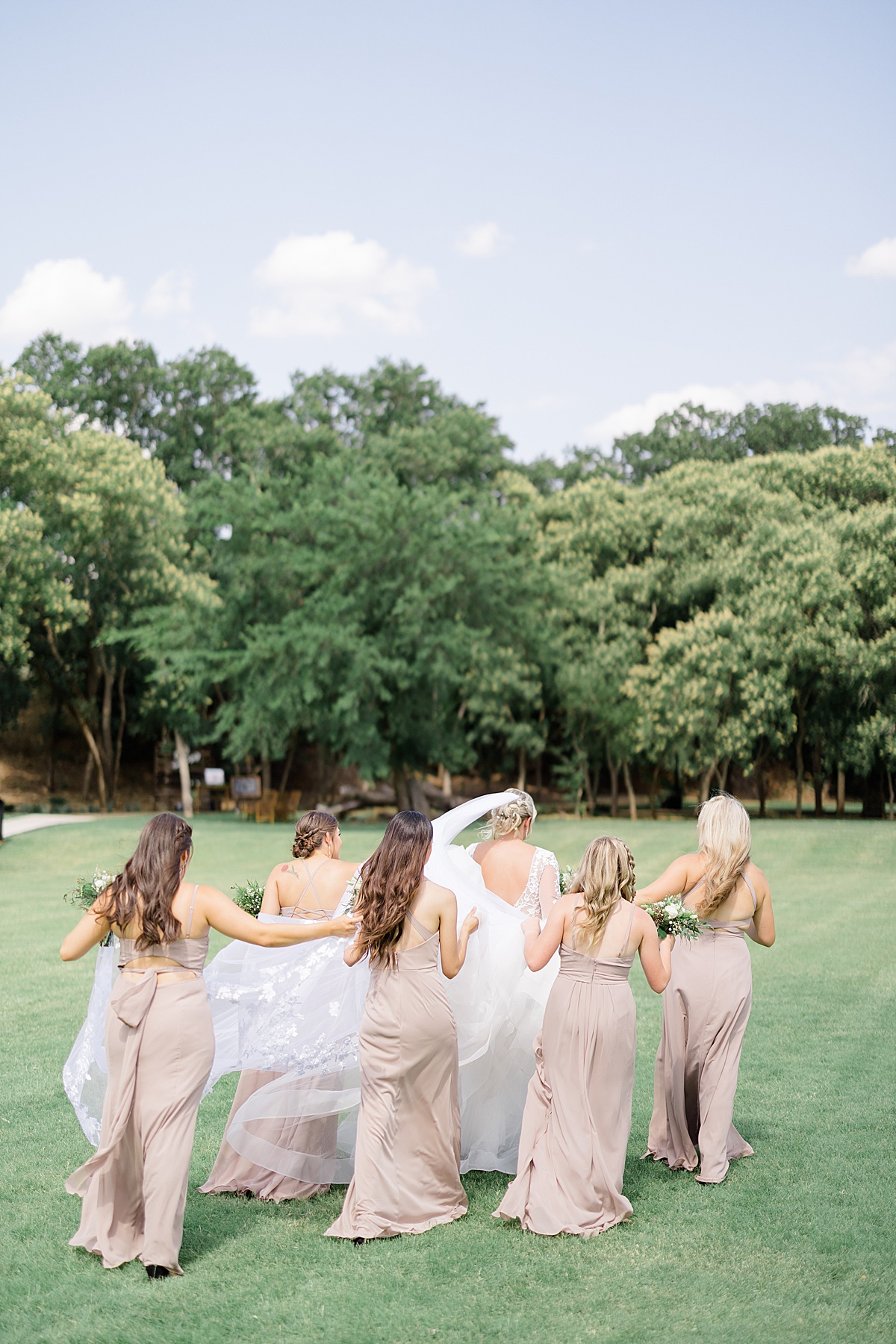 bridesmaids in taupe gowns walk across oklahoma field with bride before outdoor ceremony shot by Destination wedding photographer