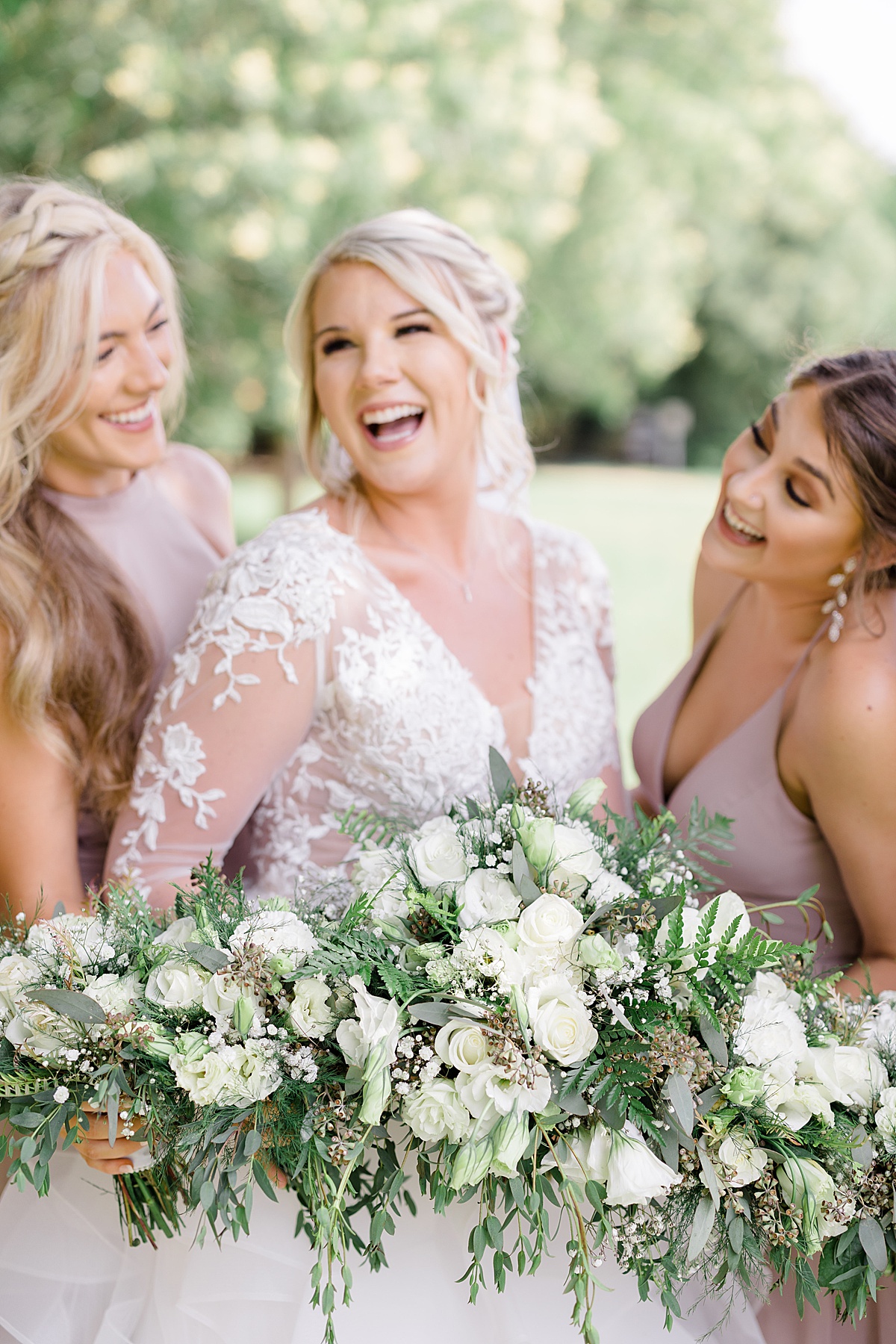 bride in lace gown poses with bridesmaids and white rose bouquets for Hunter Hennes Photography