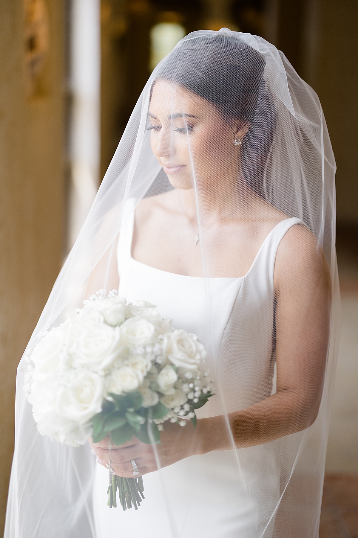 bride poses in veil with white rose bouquet before heartfelt Catholic ceremony