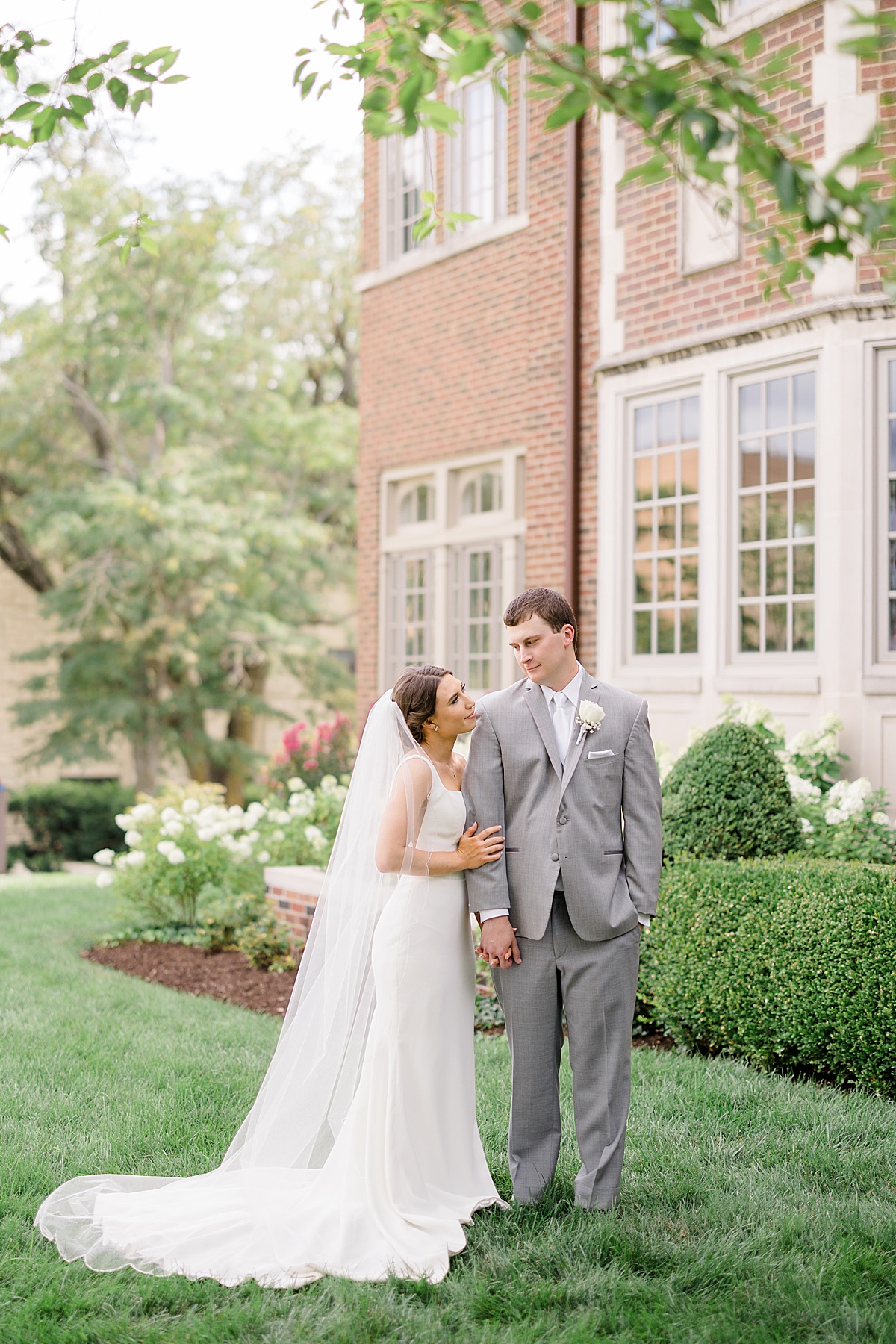 bride in minimalist wedding gown and groom in gray suit pose in garden after wedding shot by Hunter Hennes Photography