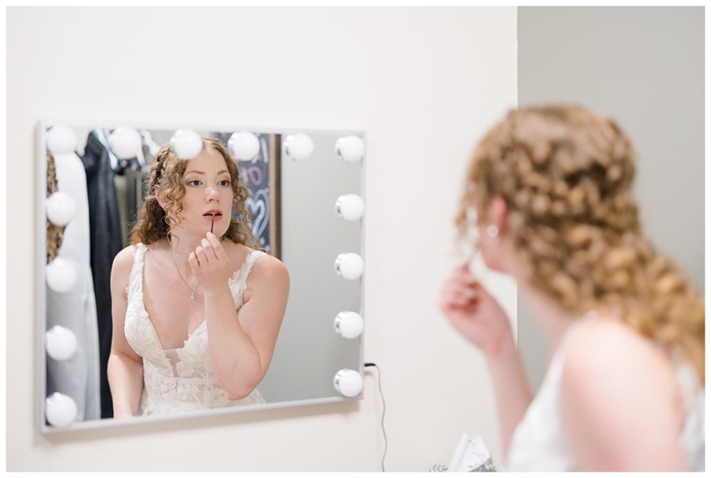 bride looks in mirror and applies lip gloss at Minnesota park wedding
