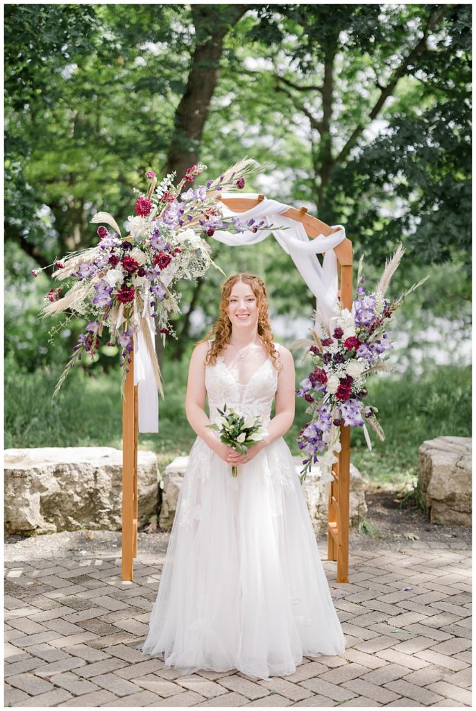 woman stands under arch decorated with flowers at Minnesota park wedding