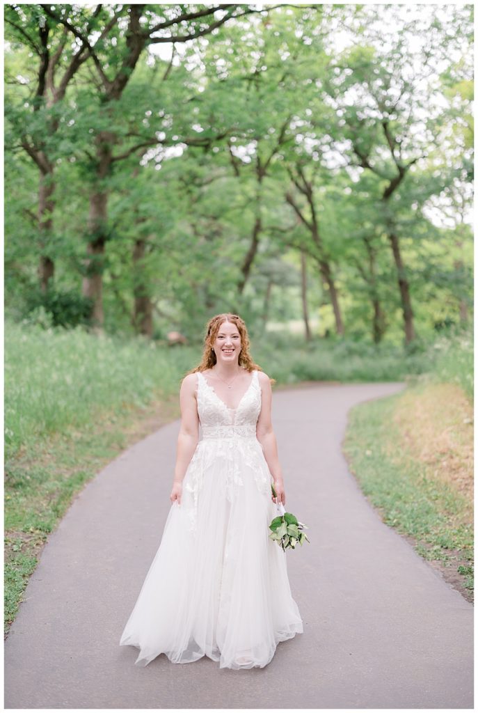 bride stands on path surrounded by greenery at Minnesota park wedding
