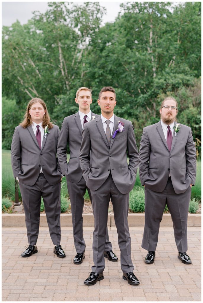 groomsmen stand together with hands in pockets outside by Hunter Hennes Photography 
