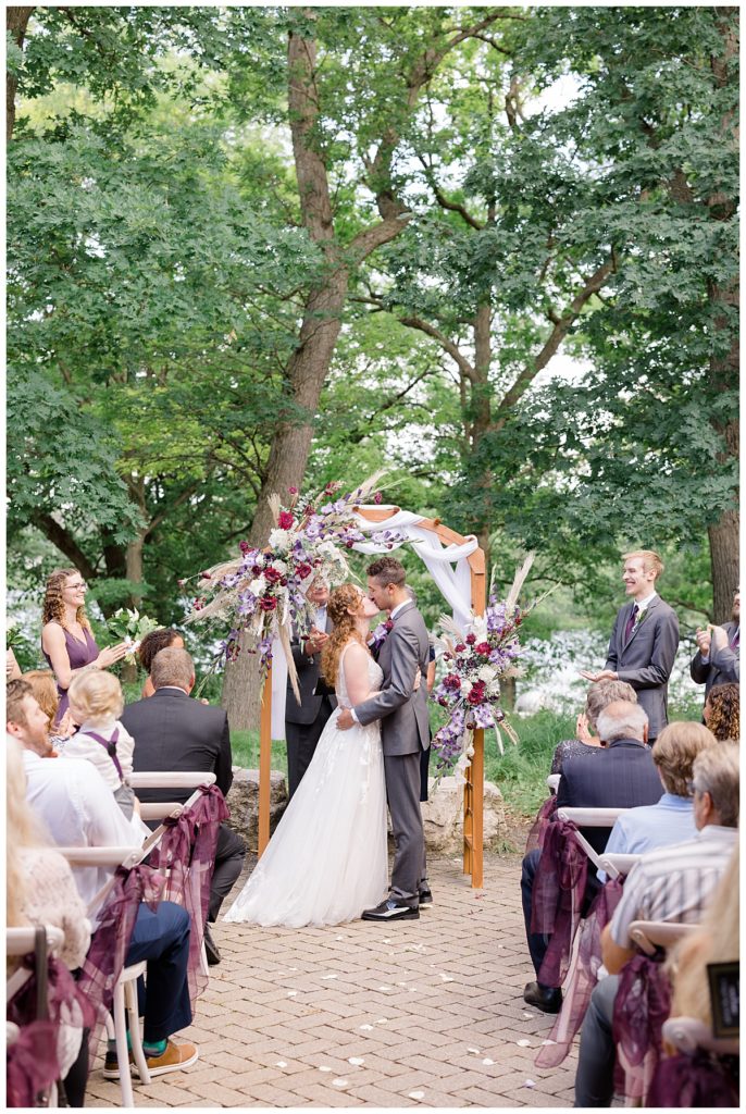 couple kisses under arch at Minnesota park wedding