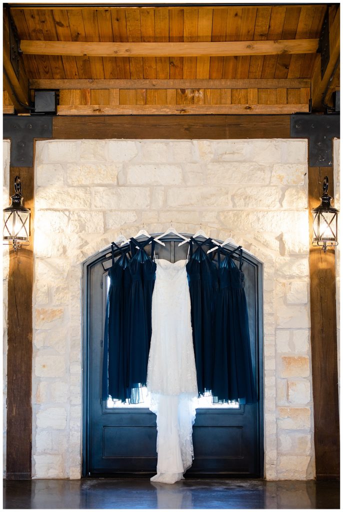 wedding and bridesmaids dresses hang on stone wall by Hunter Hennes Photography