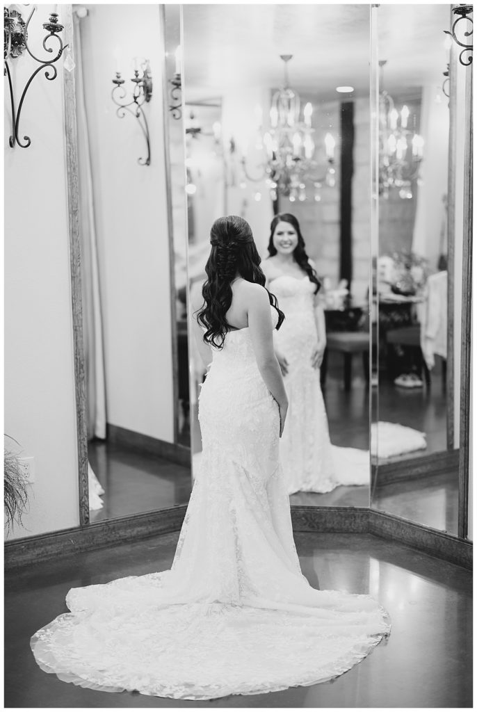bride looks at self in three panel mirror at elegant Oklahoma wedding