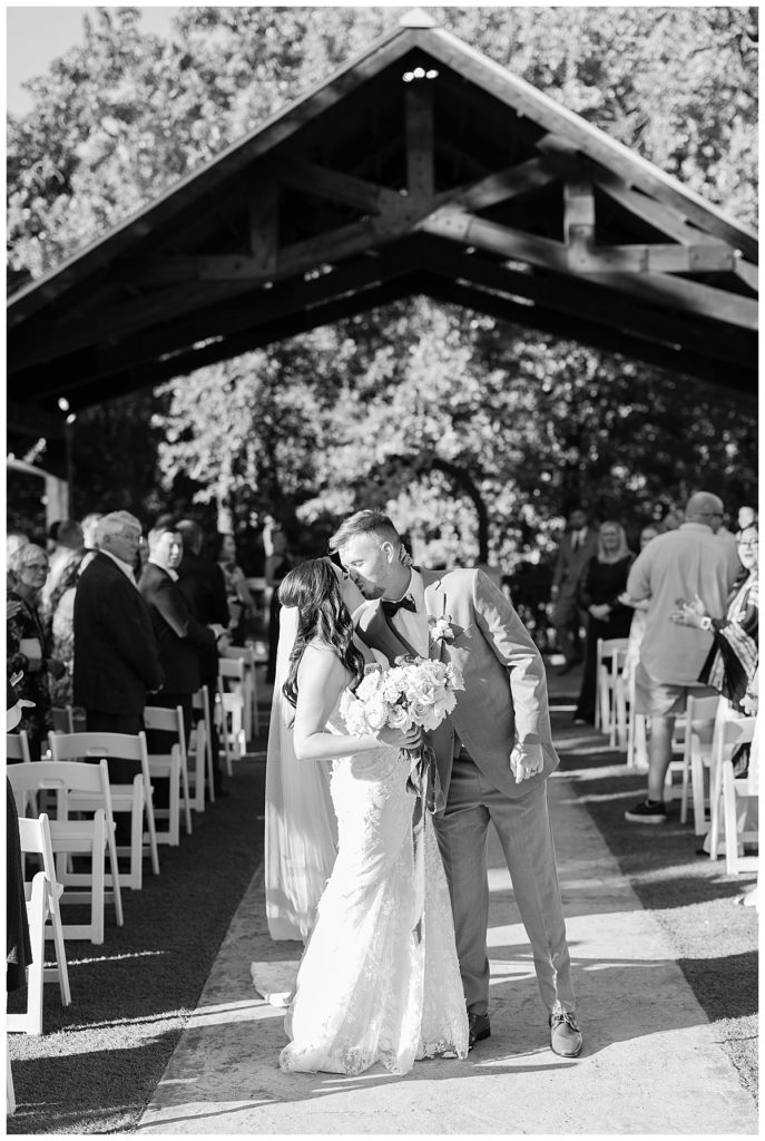 couple kisses at end of aisle at elegant Oklahoma wedding