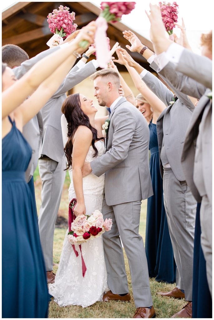 bride and groom stand under bridal party's raised hands at elegant Oklahoma wedding